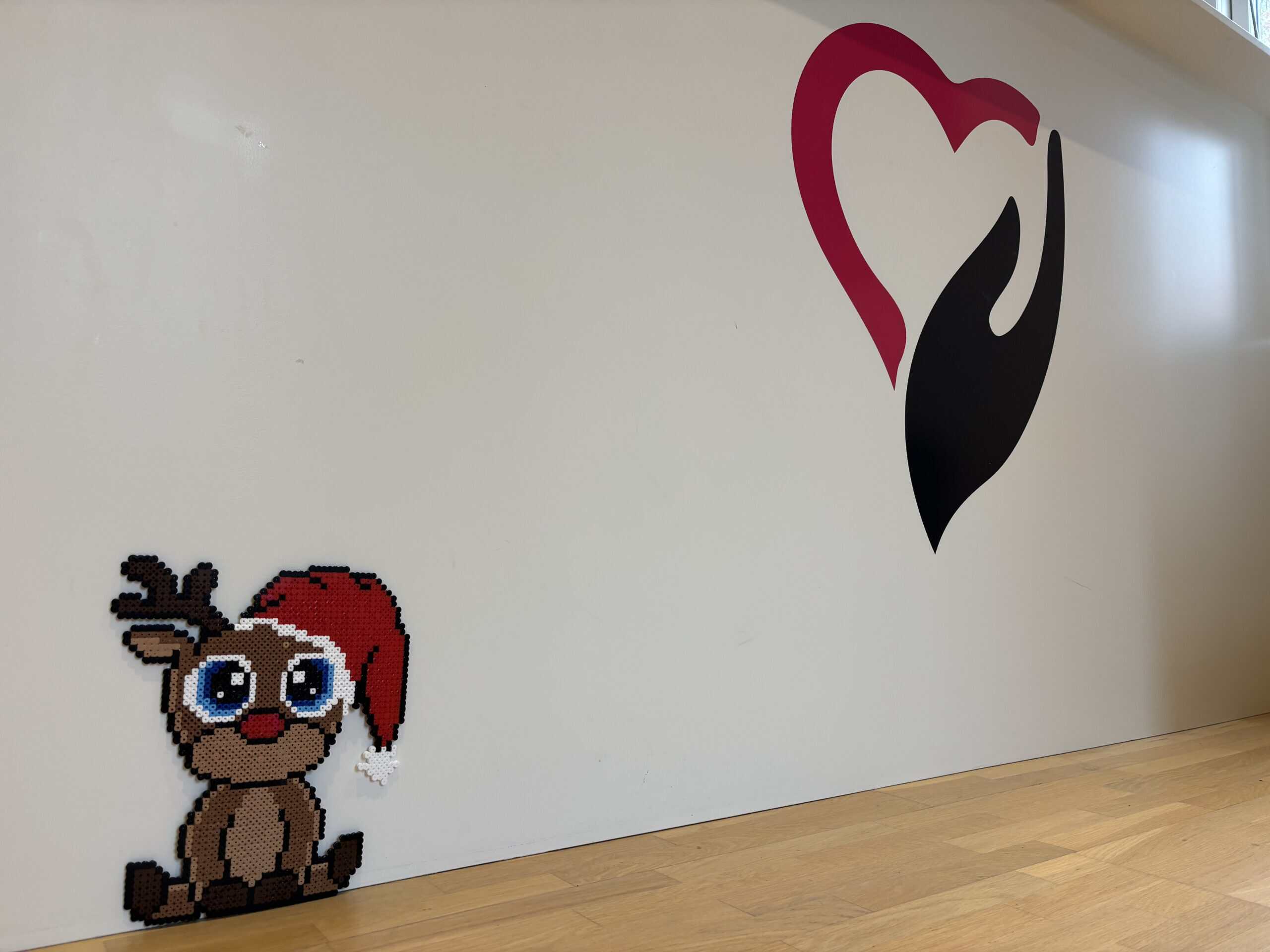 Perleplade af rensdyr med nissehue, som sidder på en væg med SundhedsHusets logo